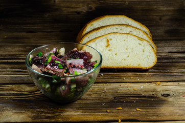 Herring with spices in glass bowl and sliced bread on wooden table