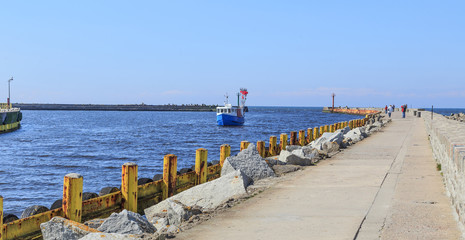Darłówek, nadmorska, portowa i kąpieliskowa dzielnica Darłowa. Kuter rybacki wpływający do portu widziany z falochronu po którym spaceruję turyści