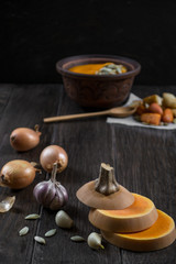 Pumpkin and ingredients for cooking over dark wooden  background.  Fresh pumpkin slice, garlic,onion. Pumpkin cream soup