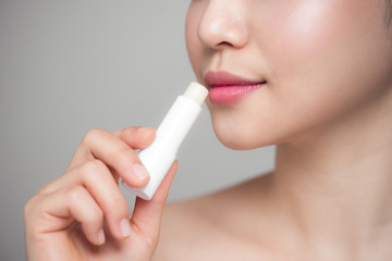 Asian woman applying hygienic lip balm over grey background - obrazy, fototapety, plakaty