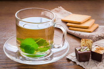 Peppermint green tea in the glass cup with cookies and chocolate candies. Herbal tea on the wooden table.