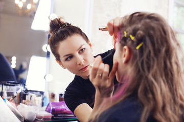 Make-up artist applying mascara on model's eyelashes, selective focus on make up artist