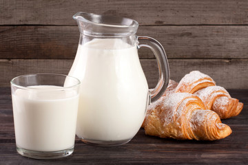 jug and glass of milk with croissants on a wooden background