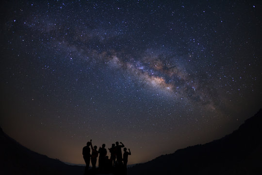 Landscape with milky way, Night sky with stars and silhouette of happy people standing on moutain, Long exposure photograph, with grain.