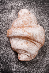 one croissant sprinkled with powdered sugar on black stone background closeup. Top view