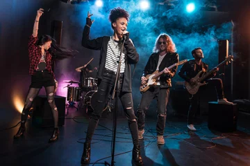 Fotobehang Female singer with microphone and rock and roll band performing hard rock music on stage © LIGHTFIELD STUDIOS