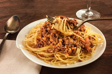 Fork of spaghetti boilognese held over plate of pasta