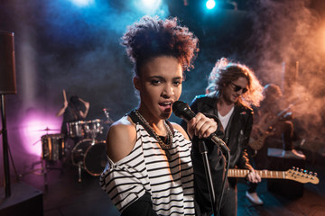 Female singer with microphone and rock and roll band performing hard rock music on stage