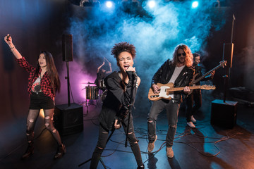 Female singer with microphone and rock and roll band performing hard rock music on stage
