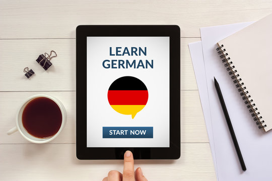 Learn german concept on tablet screen with office objects on white wooden table. All screen content is designed by me. Flat lay