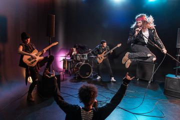 Back view of young woman gesturing rock and roll hand sign and looking at band on scene