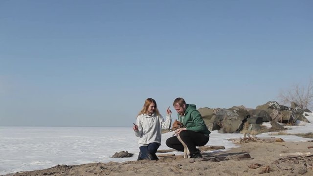 Young Couple Playing With a Dog on the Beach With Snow