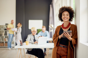 Portrait of young mixed race businesswoman. In background team working in modern office