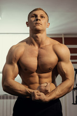 young muscular bodybuilder posing showing the biceps in the gym