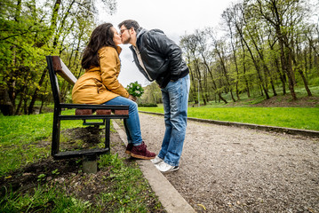 Fototapeta premium Man and woman embracing and kissing on bench in green spring park