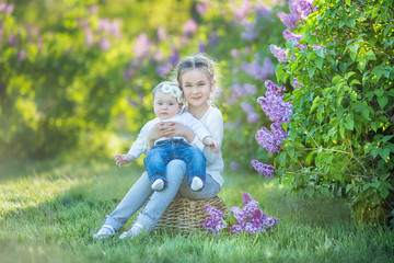 sisters with mother playing in blooming lilac garden. Cute little girls with bunch of lilac in blossom. Kid enjoying happy childhood. Family, love, peace and happiness concept