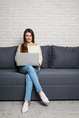 Happy pretty woman using laptop sitting on cosy sofa at home