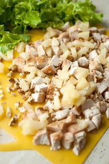 Chopped ruddy chicken breasts with leaf salad and crushed walnut on yellow cutting board.