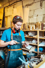 Portrait of focused  young man working in carpenting studio, filing small wooden detail
