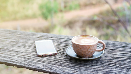 Hot coffee and smartphone on a wooden table.