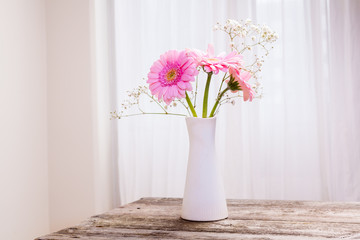 vacker bukett med rosa gerbera i vit vas på trä bord och vit gardin i bakgrunden