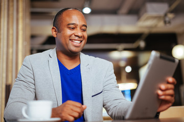 Image of happy young african man using digital tablet in cafe