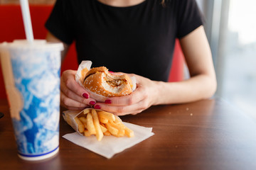 Young girl holding in female hands fast food burger, american unhealthy meal on blue background, mockup with copy space for text message or design, hungry human with grilled hamburger front view