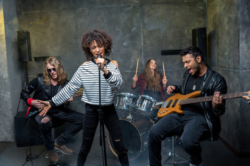 Young multiethnic rock and roll band rehearsing in musical studio