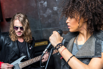 side view of woman singing in microphone with man playing guitar, rock and roll girl concept