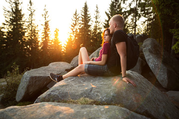 Couple man and woman sitting on cliff enjoying mountains landscape. Male and female hikers