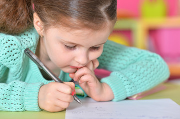Naklejka premium Little girl writing while sitting at table