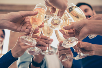 Cropped under view of friends cliking the glasses of bubbling champagne to celebrate an event...