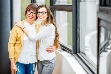 Portrait of a smiling mother and daughter standing together indoors near the window