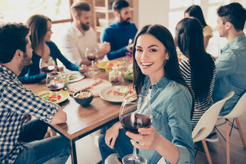 Close up of a girl looking at the camera holding glass of red wine and smiling. She is posing to photographer to memorise a moment of party