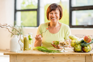 Portrait of a beautiful older woman with green healthy food on the table indoors on the window...