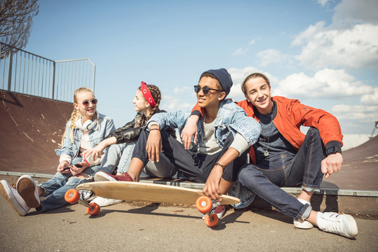 Happy teenagers group sitting together and talking at skateboard park
