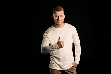 front view of handsome redhead man showing thumb up isolated on black