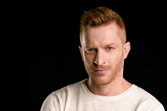portrait of handsome redhead man looking at camera  isolated on black