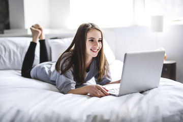 Teenage Girl Lying On Bed Using A Laptop