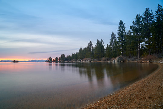 Sunset at Lake Tahoe with sand beach, mountains covered by snow at background