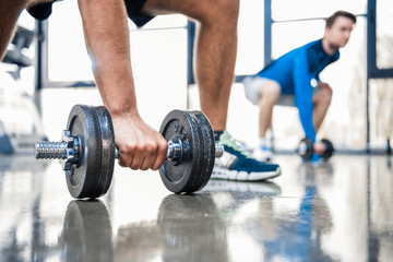young men workout with dumbbells at gym, focus on man holding dumbbell