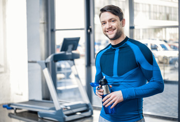 Naklejka na ściany i meble Handsome young man with bottle of water resting at gym