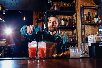  Bartender hipster with a beard makes an alcoholic cocktail behind the counter in the bar.