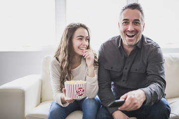 Portrait of a young man and daughter watching TV while eating popcorn on the sofa