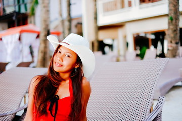 Beautiful young woman sitting on sunbed with the hat on the beach resort, summer vacation