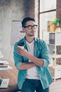 Vertical portrait of handsome businessman in casual clothes holding cup of fresh coffee and dreaming
