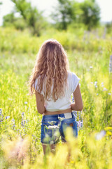 The beautiful young woman with long hair walks on a meadow