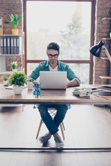 Vertical photo of handsome young guy in jeans and shirt working with computer and thinking over business project development