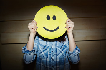 Successful female designer expressing happiness with help of smiling emoji mask while standing in...