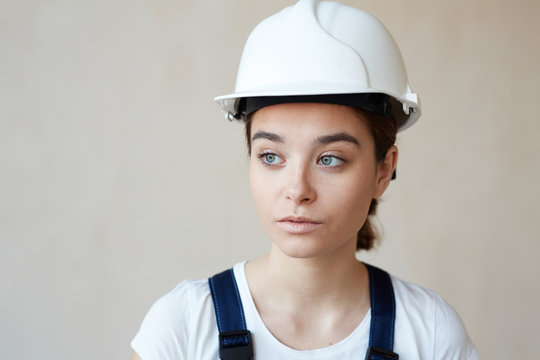 Portrait of female construction worker in hardhat standing against white wall background